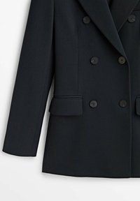 Blazer noir croisé avec larges revers, six boutons, poches à rabat et manches longues.