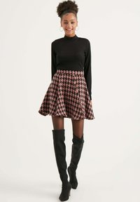 Top nero a collo alto con coste abbinato a una gonna corta a motivo houndstooth rosa. La modella indossa stivali neri con tacco alti fino alla coscia.