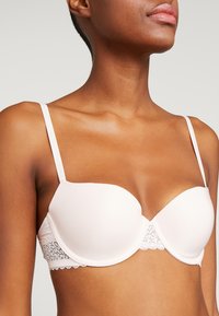 Sujetador rosa claro con copas acolchadas, borde de encaje en la base y tirantes ajustables. Textura suave con un tenue brillo.