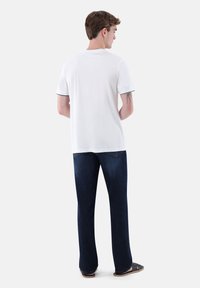 Weißes T-Shirt mit kurzen Ärmeln und schwarzem Besatz, kombiniert mit dunkelblauen Jeans. Das T-Shirt hat einen geraden Schnitt und eine weiche Textur.