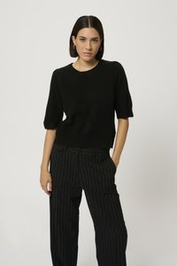 Pulover negru cu mânecă scurtă, cu o croială lejeră, realizat dintr-un material moale, asortat cu pantaloni negri cu dungi verticale, cu talie înaltă și buzunare.