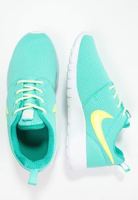 Turkossnäppor i meshtyg med vita sulor. Funktioner inkluderar gula accenter, platta snören och en strukturerad, ventilerad design.