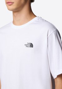 Camiseta de algodón blanca de manga corta, con un logotipo negro impreso en el lado izquierdo del pecho. Diseño clásico de cuello redondo, textura suave.