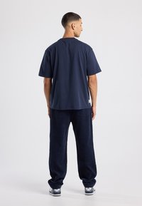 Camiseta de algodón azul marino de manga corta, combinada con pantalones de pana azul marino texturizados y zapatillas blancas con acentos azules.