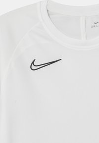 Vit idrottströja tillverkad av fuktavledande tyg, med en svart Nike-logga på vänster bröst och rundad halsringning.