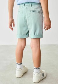 Mint green shorts with rolled cuffs, featuring back pockets and "BAKER BY TED BAKER" label. Worn with white sneakers and striped socks.