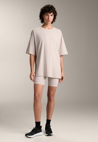 Svijetlosmeđi oversized majica kratkih rukava, uparena s odgovarajućim bež biciklističkim šortsevima i crnim sportskim cipelama s bijelim potplatima.