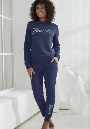 Navy blue sweatshirt and joggers set, made of soft fabric, featuring "Bench" logo in cursive on the front and leg, slim fit design.