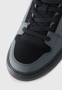 Szare i czarne trampki z gładką skórzaną i teksturowaną siateczkową cholewką, okrągłym czubkiem, czarnymi sznurowadłami oraz gumową podeszwą z wzorzystym brzegiem.