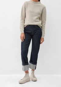 Jasno beżowy sweter prążkowany, ciemnoniebieskie dżinsy z podwiniętymi mankietami i beżowe sneakersy typu high-top, prezentujące swobodny, dopasowany wygląd.