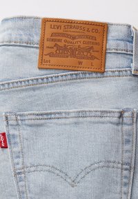 Jeans de mezclilla azul claros con una etiqueta de cuero marrón. Incluyen costuras en los bolsillos traseros y una etiqueta roja de Levi's.