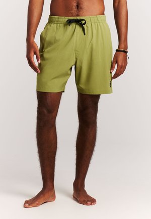 Man die lichtgroene short met trekkoord draagt, staat op blote voeten met ontspannen handen langs zijn zij, tegen een effen lichte achtergrond.