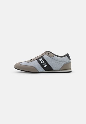 Niedriger grauer und beiger Sneaker mit schwarzer Seitenpartie, auf der das Wort "BOSS" in Weiß steht, von der Außenseite betrachtet.