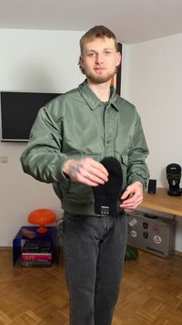 Groene satijnen bomberjack, zwarte gebreide wanten, slim-fit jeans. Gladde textuur, geribbelde manchetten aan het jack, minimale branding op de wanten.