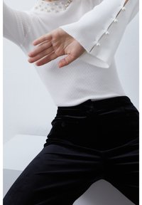 Biały prążkowany top z perłowymi ozdobami na dekolcie i mankietach, zestawiony z czarnymi welwetowymi spodniami z kieszeniami i dopasowanym krojem.