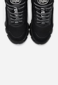 Paire de baskets Buffalo noires avec semelles épaisses, empeignes en mesh et lacets à motifs noirs et blancs sur fond blanc.