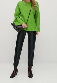 Helles grünes, übergroßes Sweatshirt mit ausgestellten Ärmeln, kombiniert mit schwarzen Lederhosen und spitz zulaufenden braunen Ankle-Boots. Minimalistische braune Tasche.