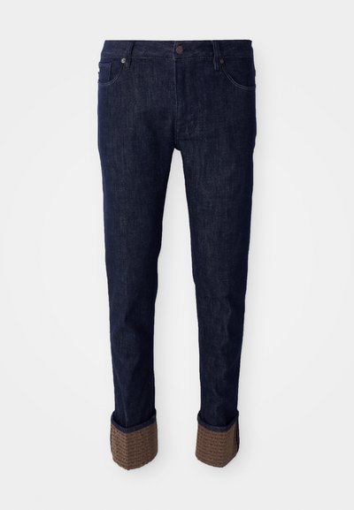 Tumed sinised teksad sirge lõikega, millel on volditud alläärid tekstureeritud pruuni materjali ja logomustriga. Tavaline viies tasku disain.