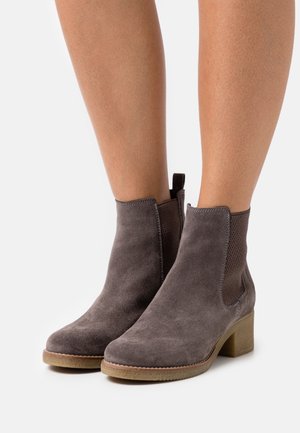 Bottines en suedine grise avec un bout rond, des panneaux latéraux élastiques et un petit talon carré. Détails texturés sur les côtés.