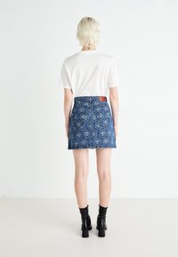 Denim mini krilo s cvetnim vzorcem, modre barve, obrubljenim robom in rjavim usnjenim oklopom, v kombinaciji z belo majico in črnimi čevlji s peto.