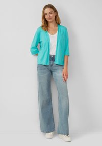 Cardigan leggero color aqua con maniche a tre quarti, design aperto anteriore, abbinato a jeans azzurri a vita alta e gamba larga e sneakers bianche.