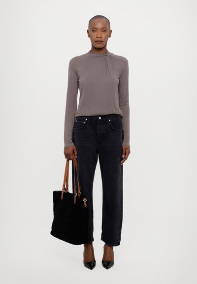 Grijze top met lange mouwen en een ronde halslijn, gecombineerd met hoge zwarte jeans. Zwarte tas met bruine handvatten en puntige zwarte hakken.