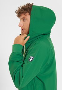 Green hooded jacket made from lightweight material, featuring a zipper, elastic cuffs, and a logo patch on the sleeve.