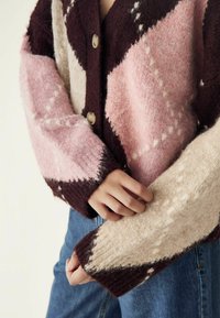 Siltā, adīta džemperis ar dimanta rakstu bordo, rozā un bēšā krāsā. Ar pogām, teksturētu audumu un kontrastējošām piedurknēm.