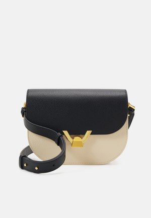 Bolso bandolera de cuero negro y beige con cierre dorado en forma de V y correa negra ajustable sobre un fondo blanco.