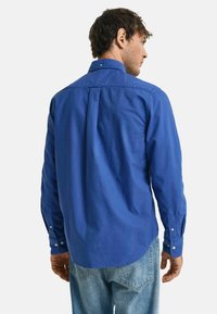 Camicia azzurra a maniche lunghe con bottoni, vestibilità slim, colletto a contrasto, texture liscia e orlo curvo. Indossata sopra jeans azzurri chiari.