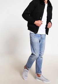 Sort bomberjakke med en faux fur-krave, parret med en hvid t-shirt, lyseblå jeans og hvide sneakers på en neutral baggrund.