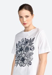 Witte katoenen t-shirt met een gedetailleerd marineblauw bloemenmotief. Korte mouwen en ronde halslijn. Gladde textuur met een casual pasvorm.