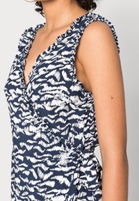 Vestido azul marino con patrón abstracto blanco, que presenta mangas con volantes y un diseño envolvente. Fabricado con tejido ligero, elegante y de textura fluida.