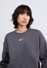 Nike sweatshirt in donkergrijs met een ribgebreide ronde hals, met een klein wit logo op de borst. Zachte textuur en een ontspannen pasvorm.