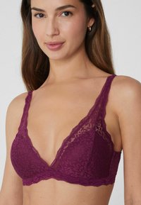 Krajkový bralette v tmavě fialové barvě s trojúhelníkovým designem, vlnitými okraji a nastavitelnými ramínky, zdobený květinovým vzorem po celé ploše.