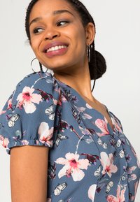 Blusa floral com mangas curtas bufantes, decote em V, e um fundo azul com flores rosas e brancas e padrões de borboletas.