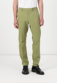 Pantalones ajustados de color verde claro, hechos de tela suave, con corte recto, bolsillos laterales y cremallera, combinados con zapatos negros.