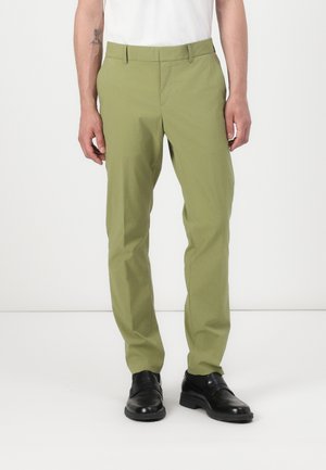 Light green tailored pants made of smooth fabric, featuring a straight cut, side pockets, and a zipper fly, paired with black shoes.