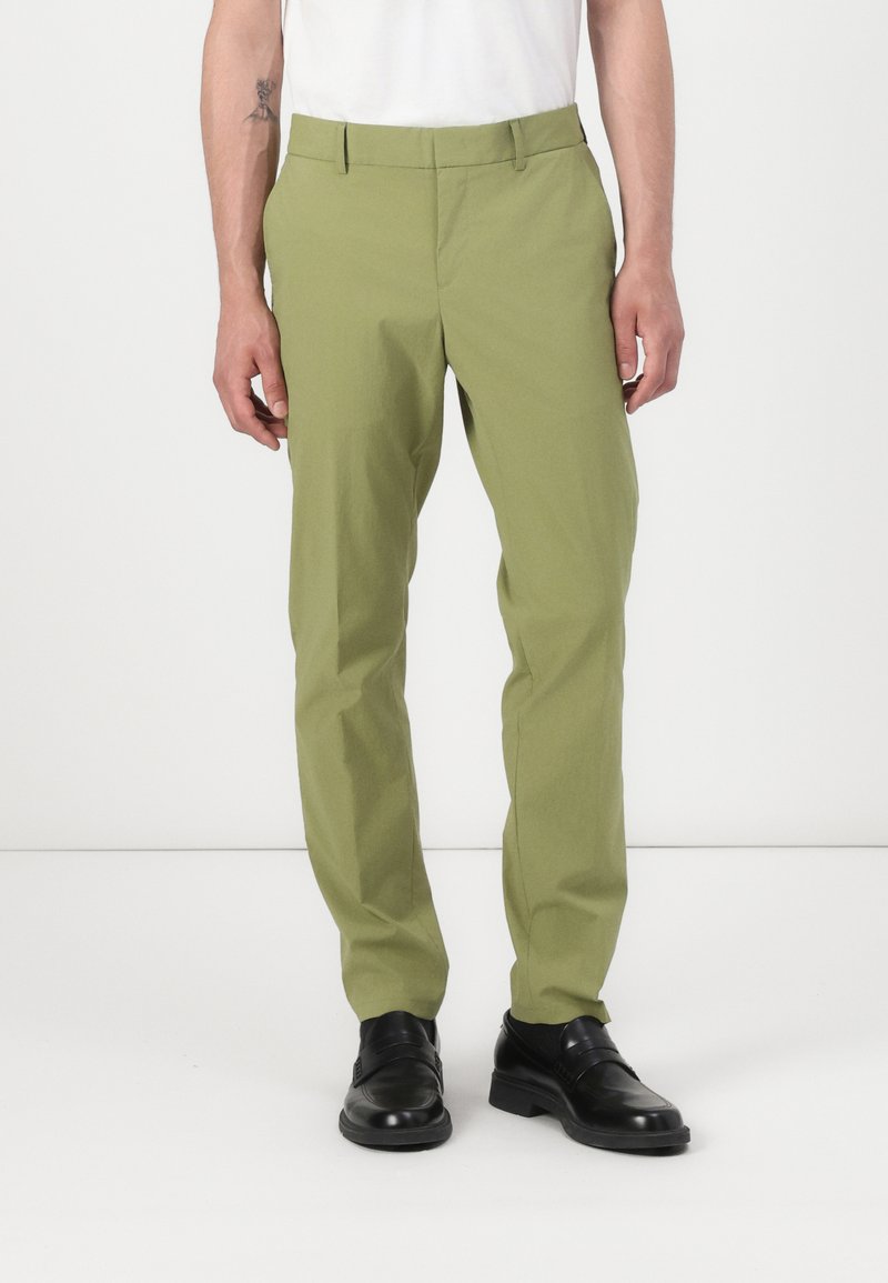 Pantalones ajustados de color verde claro, hechos de tela suave, con corte recto, bolsillos laterales y cremallera, combinados con zapatos negros.