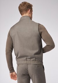 Graue Weste mit hohem Kragen und gerippten Bündchen. Der Stoff zeichnet sich durch eine feine Textur aus und wird mit einer passenden, eng geschnittenen Hose kombiniert.