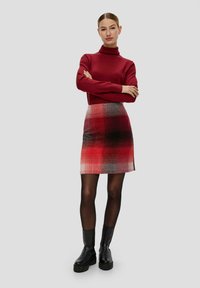 Czerwony sweter z golfem w połączeniu z mini spódnicą w kratę w odcieniach czerwieni, czerni i szarości, uzupełniony czarnymi botkami za kostkę.