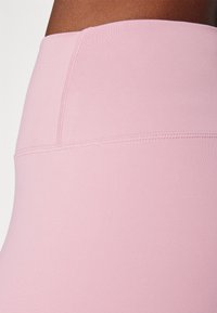 Jasnoróżowe legginsy z wysokim stanem, wykonane z gładkiego, elastycznego materiału i z płaskimi szwami, odpowiednie do aktywności fizycznej lub codziennego użytku.