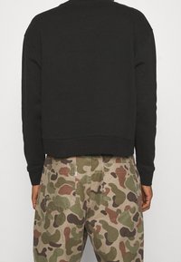 Black sweatshirt with ribbed hem and cuffs, paired with beige camouflage-patterned trousers featuring multiple pockets.