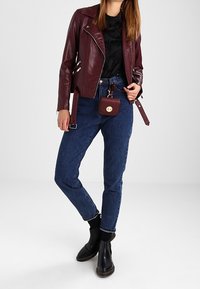 Veste en cuir bordeaux de biker, top noir à volants, jeans en denim bleu, bottes noires à chevilles et sac bandoulière assorti. Design classique, coupe ajustée.