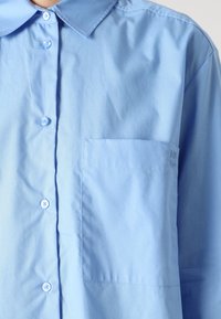 Light blue button-up shirt made of smooth fabric, featuring a pointed collar and a single chest pocket. Buttons are matching in color.