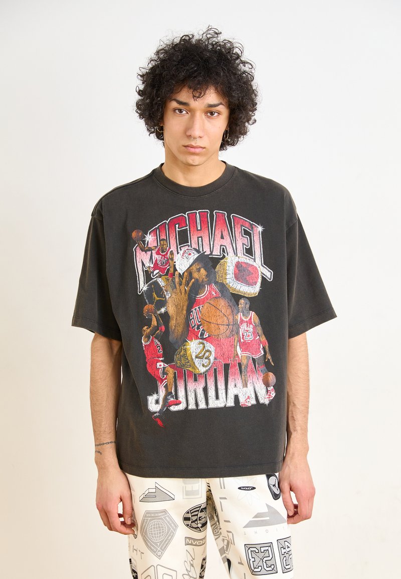 Camiseta negra de gran tamaño con un gráfico de Michael Jordan rodeado de balones de baloncesto y anillos. El tejido parece suave y tiene un aspecto vintage desgastado.
