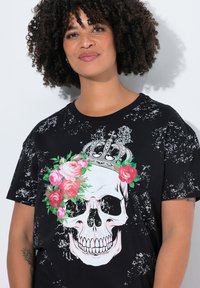 T-shirt noir avec un design graphique d'un crâne couronné de roses. Le matériau présente un motif texturé et usé.