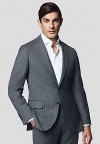 Szary garnitur w prążki z klapami notch, dwoma przednimi kieszeniami i jednoprzyciskowym zapięciem, zestawiony z białą koszulą.