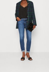 Kostkovaný blejzr v zelené a námořnické modři, černá krajková top s ramínky, modré úzké džíny, černé pletené sandály na podpatku a černá texturovaná psaníčko.