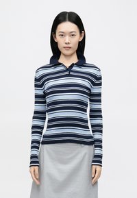 Ριγέ πλεκτό πόλο μπλουζάκι με οριζόντιες ρίγες σε ναυτικό μπλε, ανοιχτό μπλε και λευκό, με ριμπ υφή, μακριά μανίκια και γιακά στο λαιμό.